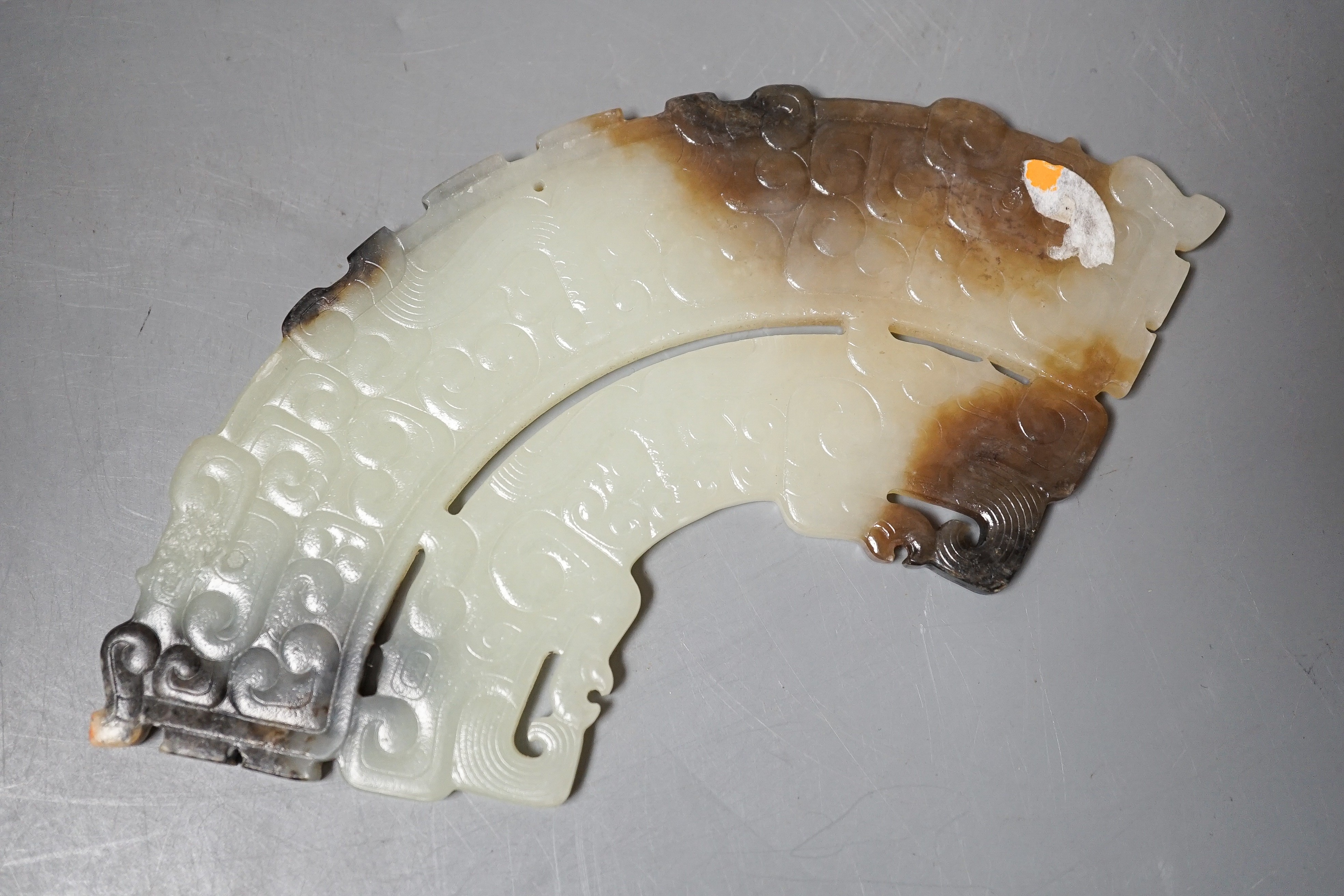 A Chinese archaistic jade fan shaped plaque, the pale celadon stone with brown and black inclusions, carved in low relief with taotie masks and leiwen, width 14.7cm